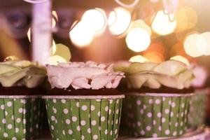 mariage petits gâteaux avec coloré arrose dans vert tasse avec guirlande lumières bokeh Contexte photo