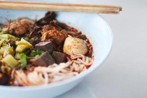 riz nouilles avec épicé porc sauce dans blanc bol avec baguettes et cuillère. thaïlandais épicé aliments. photo