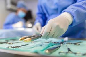 main d'infirmière prenant un instrument chirurgical pour un groupe de chirurgiens chez un patient opérant en arrière-plan dans un bloc opératoire. instruments médicaux en acier prêts à l'emploi. concept de chirurgie et d'urgence photo