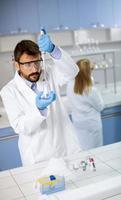Jeune chercheur en vêtements de travail de protection debout dans le laboratoire et flacon d'analyse avec liquide