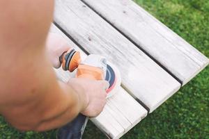 homme polis le planche sur le banc. homme réparer banc dans le jardin photo