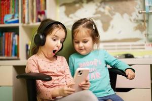 deux soeurs de petites filles portent des écouteurs en regardant des dessins animés ou des vidéos d'enfants sur leur téléphone portable. photo