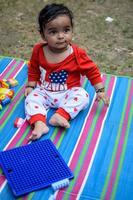 mignonne peu Indien bébé séance profiter Extérieur tirer à société parc dans Delhi, mignonne bébé garçon séance sur coloré tapis avec herbe autour, bébé garçon Extérieur tirer photo