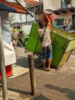 surabaya, Indonésie - avril, 2023 - une éboueur qui jette des ordures dans le poubelle Chariot photo