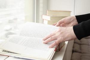 une la personne en train de lire livres près le la fenêtre. mains se tourne plus de livre page. photo