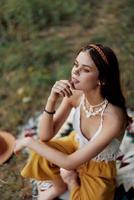 Jeune magnifique hippie femme séance sur le sol dans la nature dans le tomber dans éco Vêtements dans le le coucher du soleil lumière, une mode de vie de Voyage et harmonie avec le monde photo