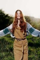 femme en marchant sur le herbe dans la nature souriant dans ferme vêtements avec magnifique cheveux en volant dans le vent content dans le des rayons de été le coucher du soleil lumière photo