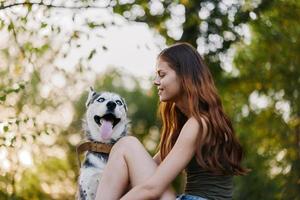 une femme avec une rauque race chien sourit et affectueusement coups sa bien-aimée chien tandis que en marchant dans la nature dans le parc dans l'automne contre le toile de fond de le coucher du soleil photo