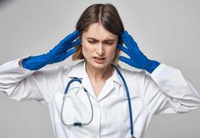 émotif femme dans bleu médical gants touche sa tête avec sa mains sur une lumière Contexte photo