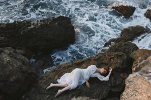 pieds nus femme dans une isolé place sur une sauvage rocheux côte dans une blanc robe vue de au dessus photo