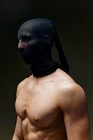 Masculin bodybuilder dans une noir masque sur une foncé Contexte tondu vue de pompé en haut bras muscles photo