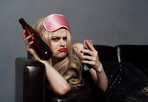 une femme dans une rose masque mensonges sur le canapé avec une bouteille de Bière et une téléphone dans sa main photo