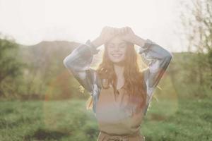 une femme jardinier dans un tablier des stands dans une champ de vert herbe en plein air, souriant sur une été après midi dans une ensoleillé le coucher du soleil après une jours travail photo