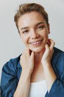 une Jeune femme séance dans une chaise à Accueil souriant avec les dents avec une court la Coupe de cheveux dans jeans et une denim chemise sur une blanc Contexte. fille Naturel pose avec non filtres photo