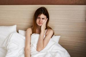 femme réveillé en haut de bonne heure dans le Matin et toucher sa visage avec sa mains en dessous de le couvertures dans lit photo