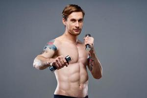 nu athlète avec une tatouage et haltères dans mains téléphone aptitude la musculation photo