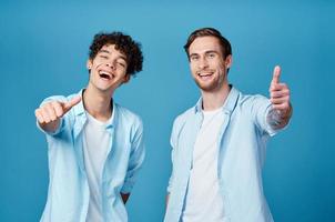 deux copains dans identique chemises et une T-shirt faire des gestes avec leur mains sur une bleu Contexte photo