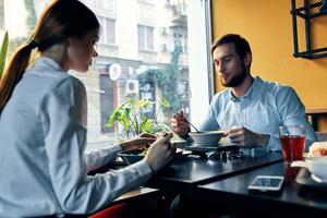 une femme dans une lumière chemise et une affaires homme avoir le déjeuner à une table dans une café délicieux nourriture les boissons des employés photo