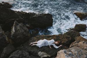 magnifique Jeune femme dans une blanc robe mensonge sur une pierre dans une blanc robe vue de au dessus photo