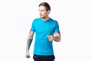 homme dans bleu T-shirt avec haltères dans main tatouage aptitude faire des exercices photo