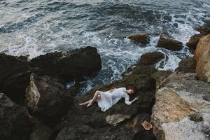 femme dans une isolé place sur une sauvage rocheux côte dans une blanc robe vue de au dessus photo