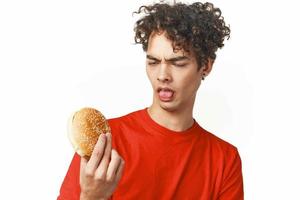 aux cheveux bouclés gars vite nourriture dans le mains de une casse-croûte nourriture régime lumière Contexte photo