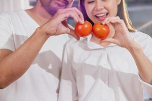 Jeune asiatique couple cuisine avec des fruits et des légumes et en utilisant portable dans le cuisine à cuisinier nourriture ensemble dans le famille Heureusement, famille concept. photo