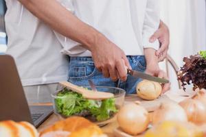 Jeune asiatique couple cuisine avec des fruits et des légumes et en utilisant portable dans le cuisine à cuisinier nourriture ensemble dans le famille Heureusement, famille concept. photo