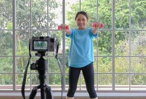 content Jeune asiatique femme levage haltères exercice et vivre diffusion avec souriant affronter. magnifique sourire Jeune asiatique femme exercice à maison. Jeune gens national la vie concept. sélectif se concentrer. photo