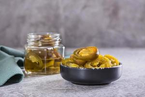 tranché mariné jalapeno poivrons dans bol et verre pot sur table photo