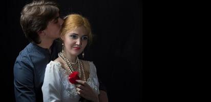 magnifique couple dans rétro style. une homme câlins une femme. fille dans une blanc robe avec une rouge Rose sur une Contexte de une homme. photo