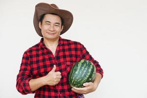 Beau asiatique homme porte chapeau, rouge plaid chemise, détient pastèque fruit. concept, agriculture profession, thaïlandais agriculteur, grandir et vendre pastèque des fruits comme économique surgir photo