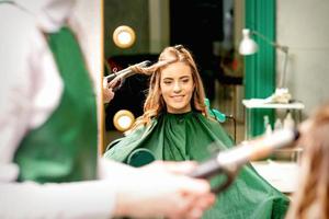 coiffeur en utilisant curling pinces boucles longue marron cheveux sur le Jeune caucasien fille dans une beauté salon. photo