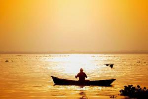 soir d'or le coucher du soleil temps, une pêcheur pêche sur le bord de mer sur une bateau. photo