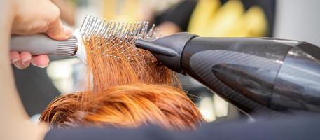 fermer de maîtrise main avec brushing et brosse à cheveux soufflant femelle rouge cheveux dans une salon. photo