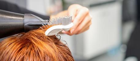 fermer de maîtrise main avec brushing et brosse à cheveux soufflant femelle rouge cheveux dans une salon. photo