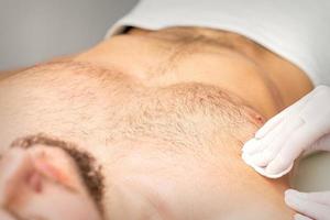 Jeune caucasien homme recevoir cheveux suppression de le sien poitrine dans une beauté salon, épilation Pour des hommes torse. photo