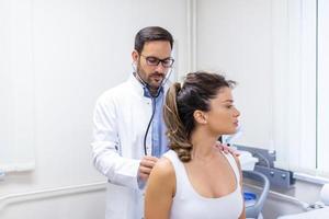 Jeune femelle patient dans le clinique souffert de pneumonie, elle est tousser le médecin écoute à le respiration sifflante dans le poumons avec une stéthoscope. photo