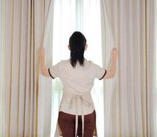 Jeune femme de chambre ouvrant les rideaux dans la chambre d'hôtel photo