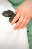 proche en haut de masseur main lingettes noir massage des pierres avec une blanc serviette. photo