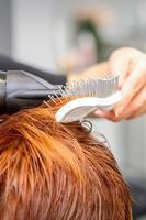 fermer de maîtrise main avec brushing et brosse à cheveux soufflant femelle rouge cheveux dans une salon. photo