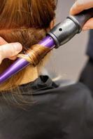 proche en haut de les coiffeurs mains en utilisant une curling le fer pour cheveux boucles dans une beauté salon. photo