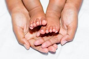 le doux jambes de une bébé mis sur le paume de le de la mère deux mains sur une blanc Contexte. photo