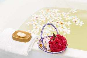 une relaxant une baignoire avec blanc plumeria fleurs. Frais Matin dans le salle de bains avec savon, serviette et fleur panier. photo