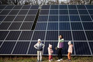 mère avec Trois des gamins sur le Contexte de solaire panneaux. éco énergie. photo