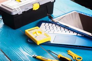 l'assistant répare l'ordinateur portable avec des outils et des mains sur la table en bois bleue. vue de dessus photo