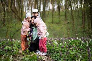 content de la mère journée. nous l'amour toi, maman. mère avec une bouquet de fleurs et Trois des gamins dans printemps épanouissement forêt. photo