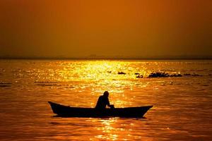 soir d'or le coucher du soleil temps, une pêcheur pêche sur le bord de mer sur une bateau. photo