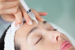 médecin appliquant un anti vieillissement faciale traitement sur Jeune femme patient en utilisant une seringue photo