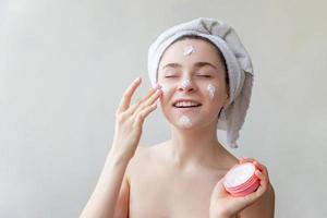 portrait de beauté d'une femme en serviette sur la tête avec un masque nourrissant blanc ou une crème sur le visage, fond blanc isolé photo